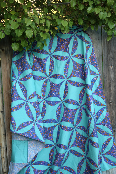 blue and teal orange peel quilt top hanging from fence